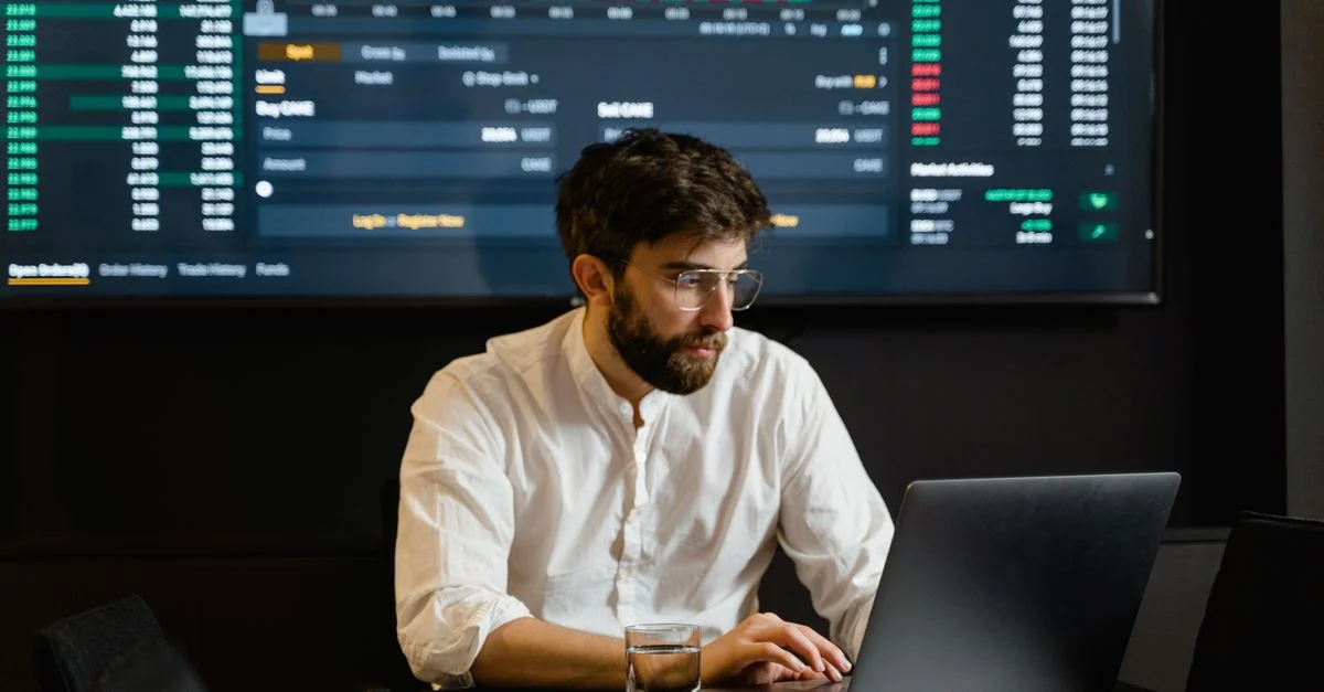 Professionnel analysant les tendances du marché boursier à l'aide d'un ordinateur portable et d'un affichage numérique dans un bureau moderne.