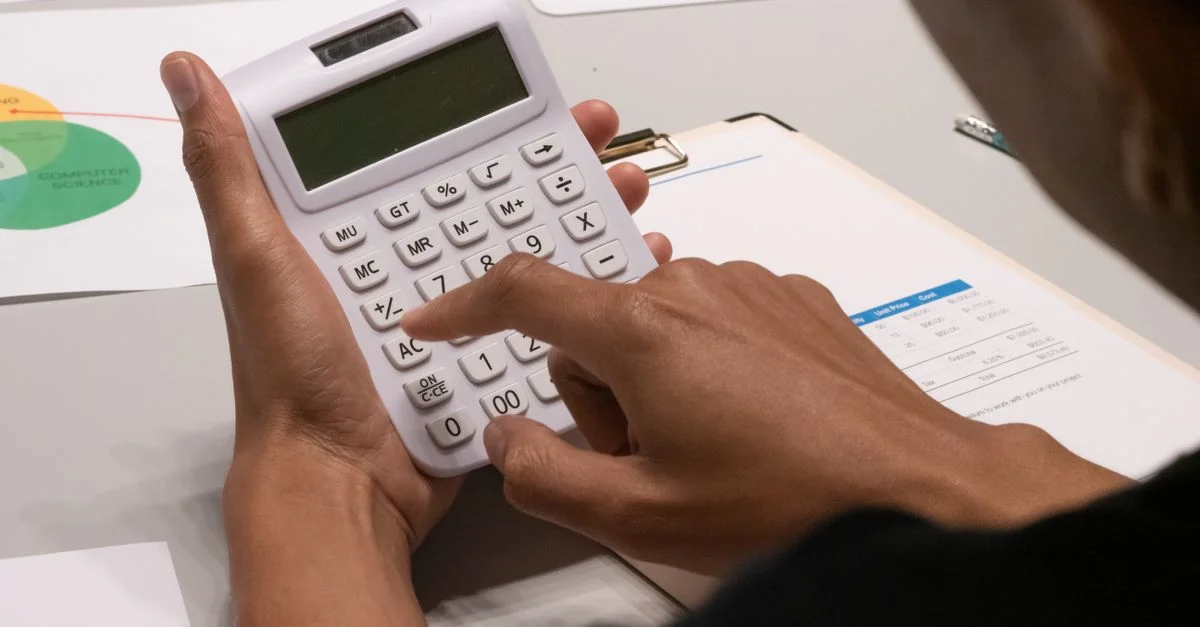 Image claire d'une personne utilisant une calculatrice au milieu de documents financiers et de graphiques.
