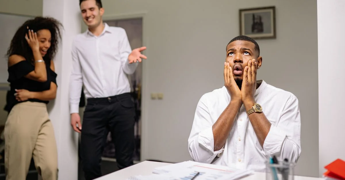 Homme d'affaires stressé avec des collègues riant dans un environnement de bureau moderne.