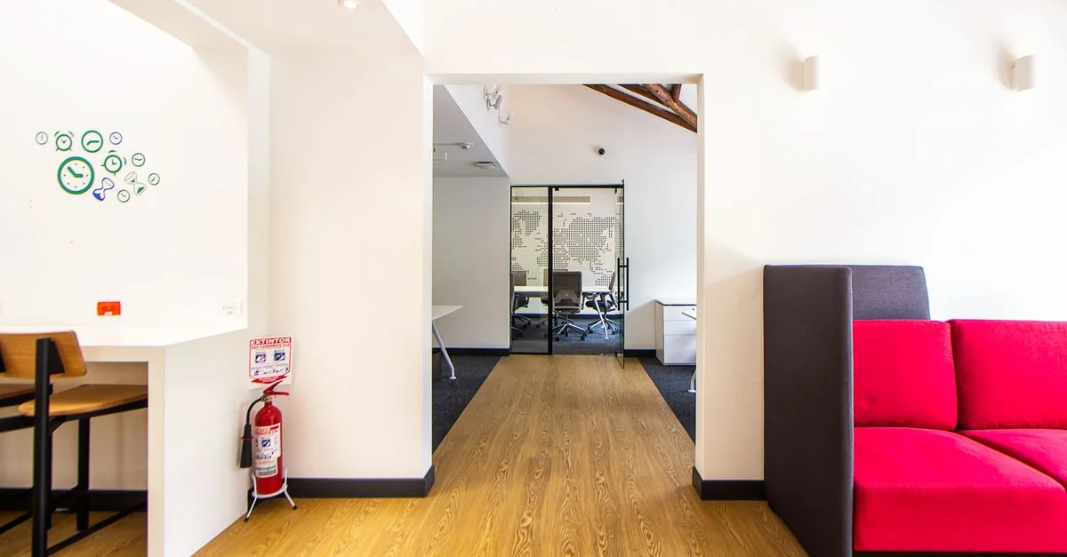 Lounge de bureau contemporain avec un canapé rouge saisissant, un sol en bois et des éléments de design minimalistes.
