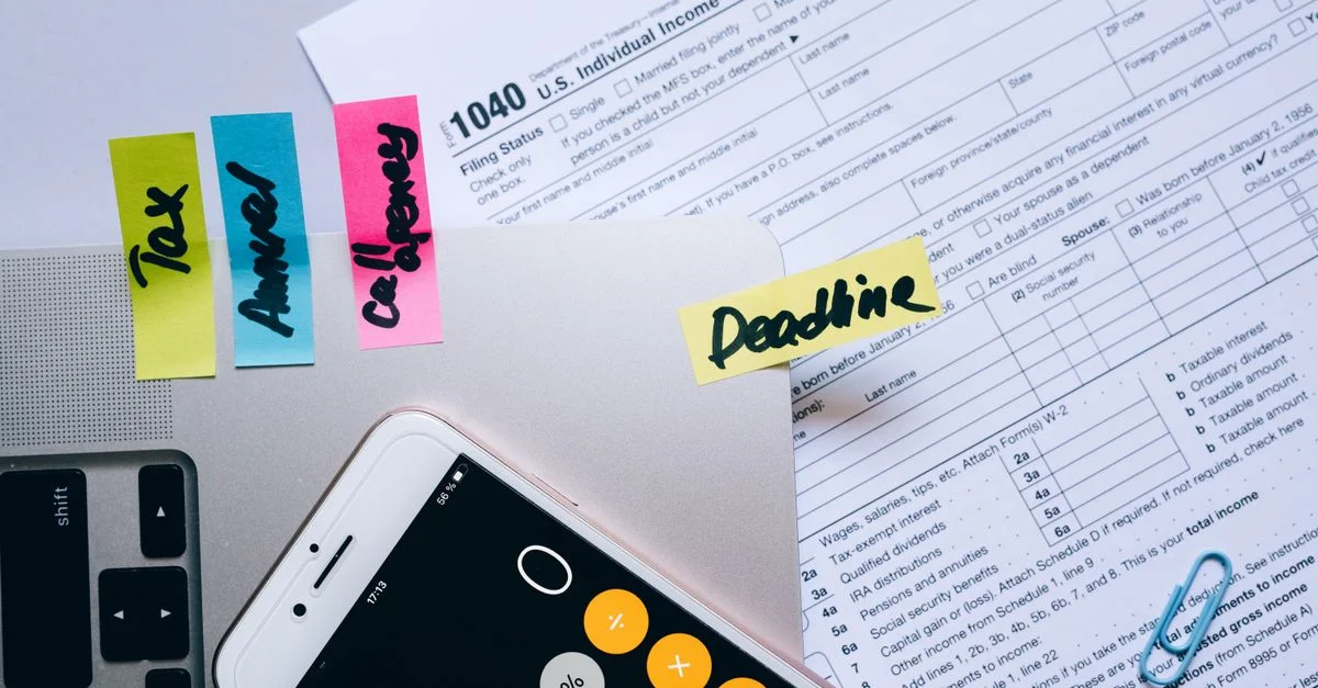 Vue aérienne de bureau montrant des documents fiscaux, une application de calculatrice sur smartphone, des notes autocollantes et des trombones.