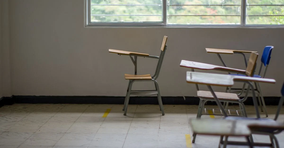 Intérieur de salle de classe calme et vide avec des bureaux scolaires près d'une grande fenêtre.