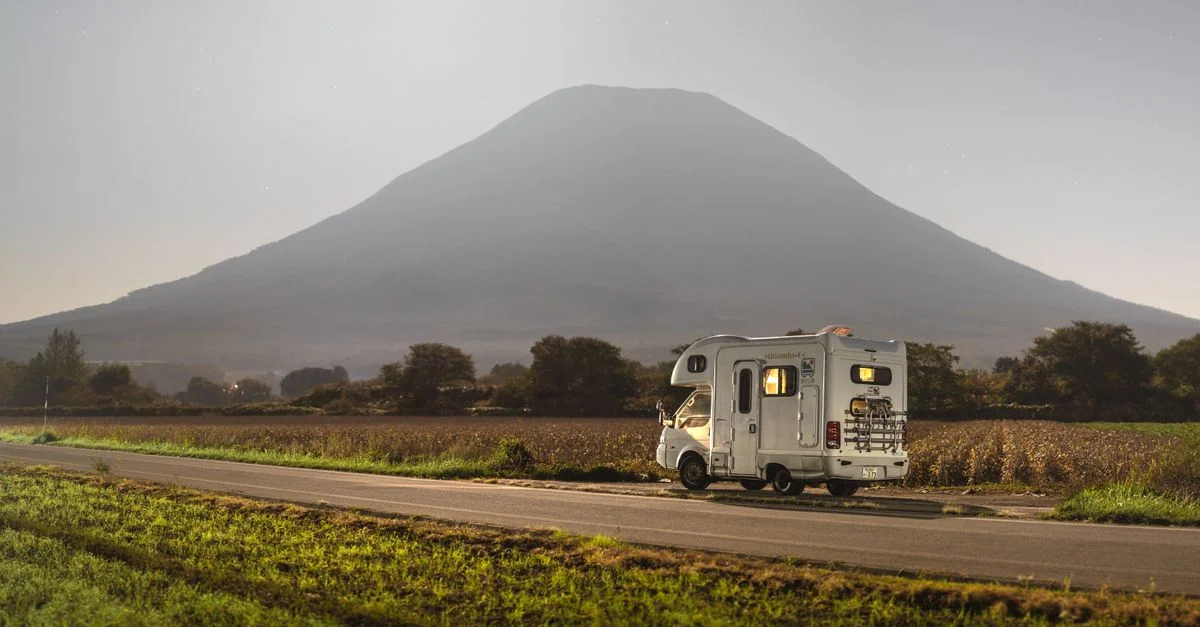 Scène tranquille d'un camping-car garé sous une montagne volcanique illuminée par la lune la nuit.