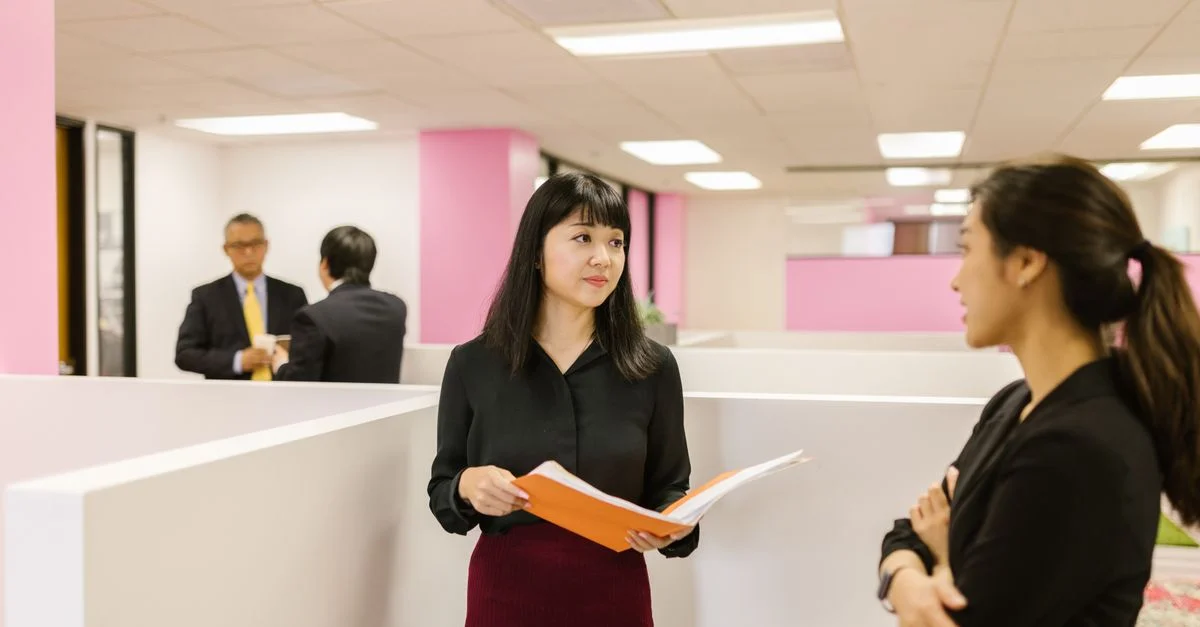 Deux femmes d'affaires discutent de documents dans un environnement de bureau moderne, mettant en avant le travail d'équipe et le professionnalisme.