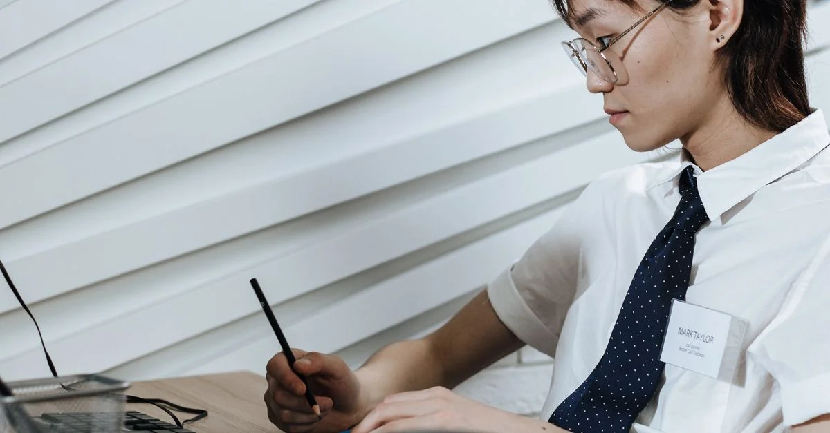 Employée de bureau portant des lunettes prenant des notes à son bureau avec un ordinateur dans un cadre moderne.