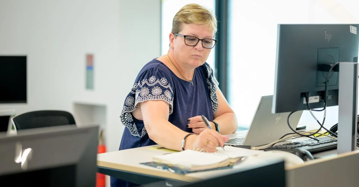 Femme professionnelle portant des lunettes travaillant à un bureau avec un ordinateur portable et un cahier.